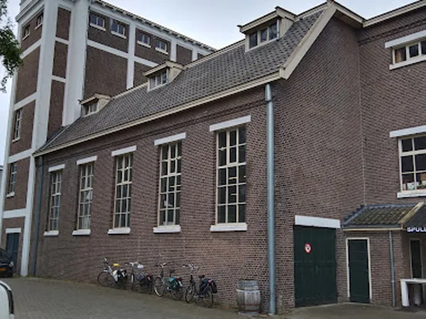 Bakstenen gevel van kringloopwinkel met grote ramen en groene deur, fietsen ernaast