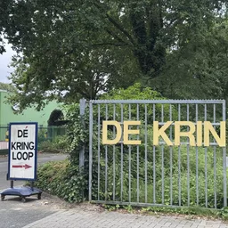 Ingang van kringloopwinkel met groen gevel, nummer 36 en poort met 'DE KRIN' tekst zichtbaar