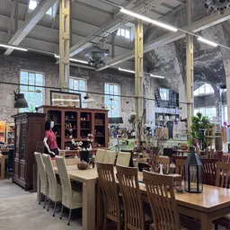 Ruim interieur van kringloopwinkel met houten meubels, tafels met stoelen, grote ramen en industrieel plafond