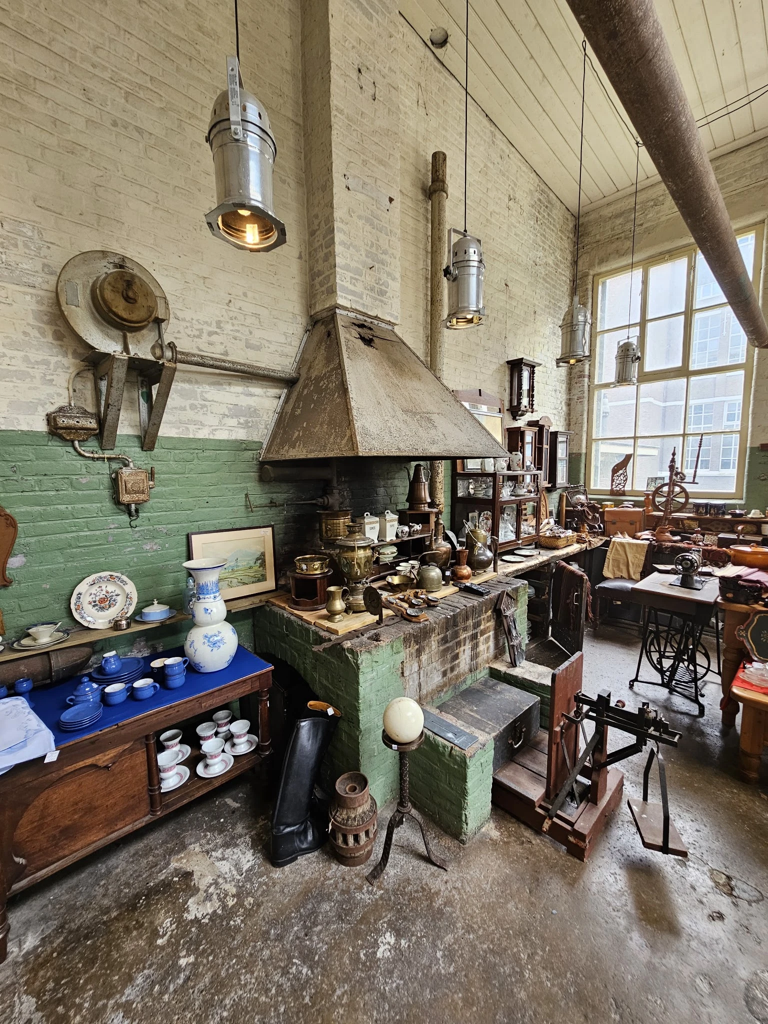 Ruim interieur van kringloopwinkel met groene muren, vintage huishoudspullen, servies en meubilair op kasten en tafels