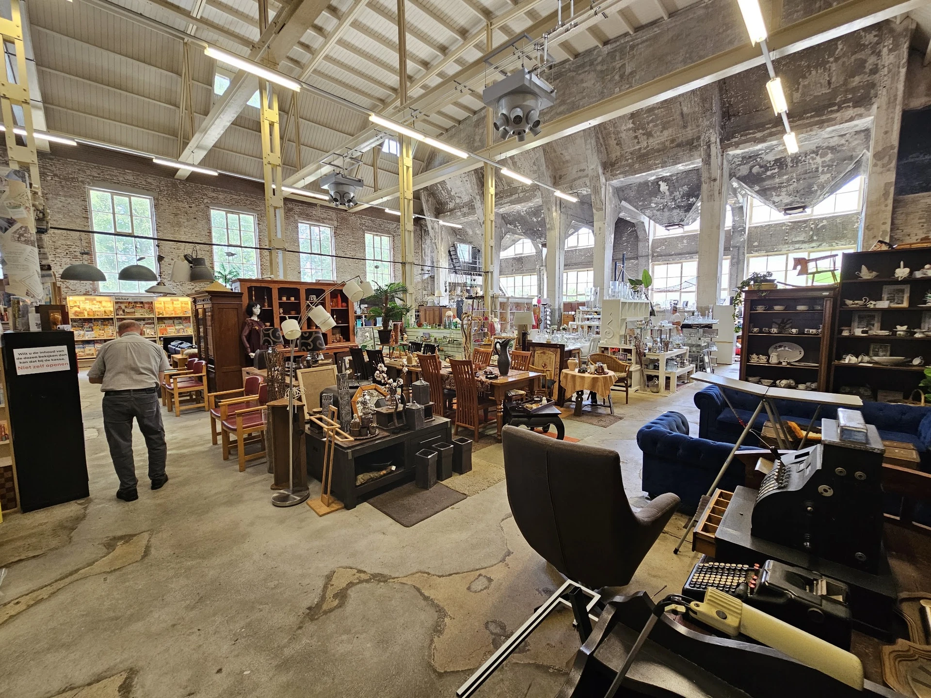 Ruim magazijnachtig interieur van een kringloopwinkel met hoogtekasten, diverse meubels, tafels en andere tweedehands spullen