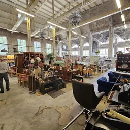Ruim magazijnachtig interieur van een kringloopwinkel met hoogtekasten, diverse meubels, tafels en andere tweedehands spullen