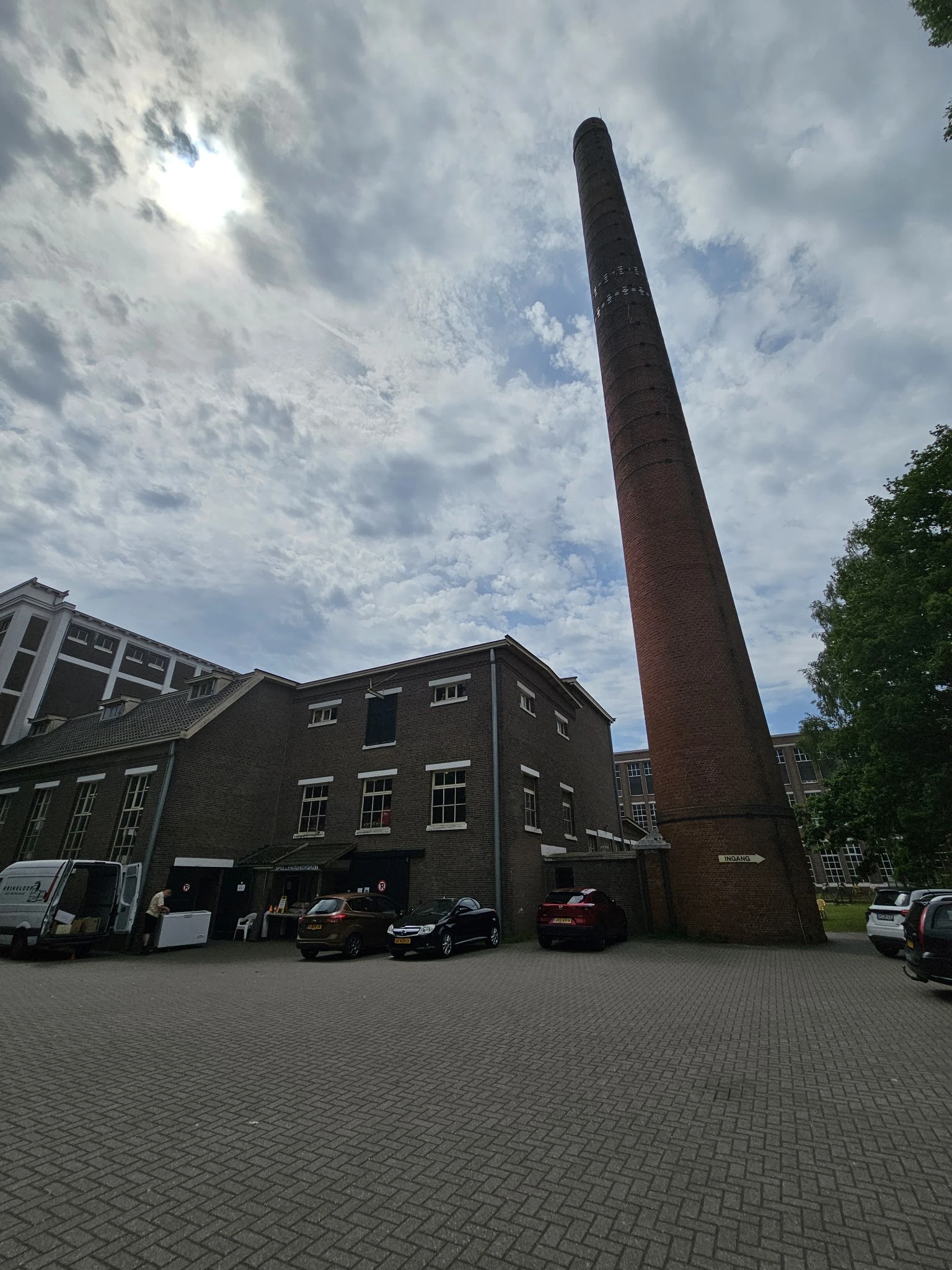 Voorgevel van een donker bakstenen kringloopwinkel met grote raampartijen en karakteristieke rode schoorsteenpijp