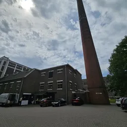 Voorgevel van een donker bakstenen kringloopwinkel met grote raampartijen en karakteristieke rode schoorsteenpijp