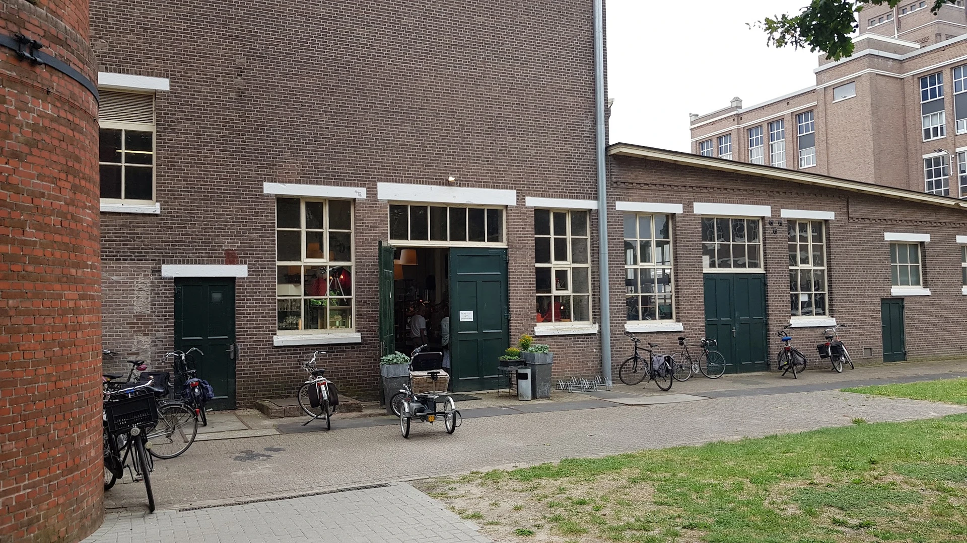 Voorkant van bakstenen kringloopwinkel met groene deuren en ramen, fietsen geparkeerd ervoor