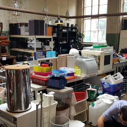 Rommelig werkgebied in een kringloopwinkel met dozen, manden, printers en diverse spullen