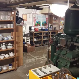 Winkelbinnenruimte met houten stellingen vol servies, vintage machine en werkplek