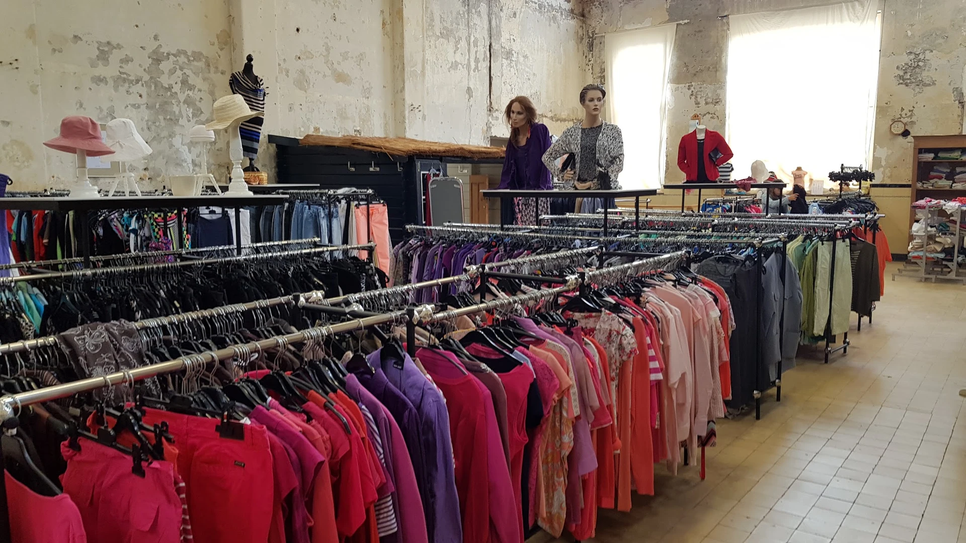 Rekken met uitgestalde tweedehands kleding in verschillende kleuren en maten in de winkel