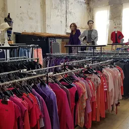 Rekken met uitgestalde tweedehands kleding in verschillende kleuren en maten in de winkel