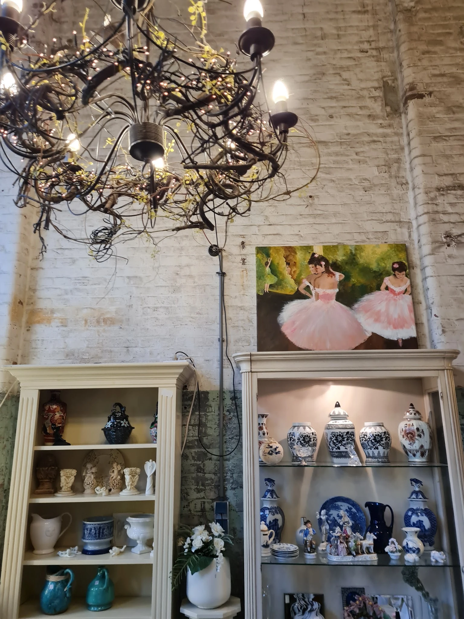 Twee wandkasten met decoratieve vazen en een schilderij van ballerina's boven elkaar aan een betonnen wand