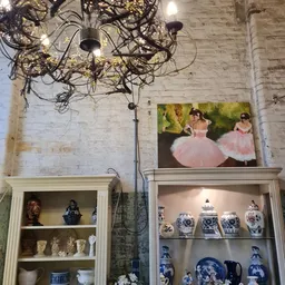 Twee wandkasten met decoratieve vazen en een schilderij van ballerina's boven elkaar aan een betonnen wand