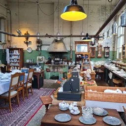 Ruim interieur van kringloopwinkel met groene muren, hanglampen, diverse meubels en spullen op tafels en rekken