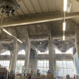 Ruim interieur van kringloopwinkel met hoge plafonds, grote ramen, verlichting en enkele bezoekers