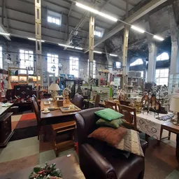 Ruim interieur van kringloopwinkel met tweedehands meubels, stoelen, tafels en kussens uitgestald tussen grote raampartijen