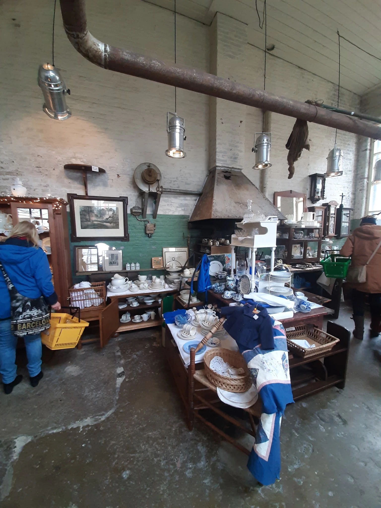 Interieur van kringloopwinkel met stellingen vol servies, huishoudartikelen en andere goederen, hanglampen en oude foto's aan