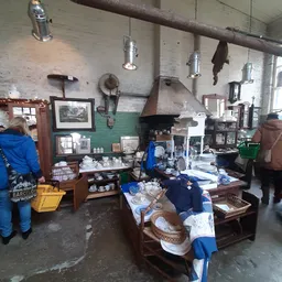 Interieur van kringloopwinkel met stellingen vol servies, huishoudartikelen en andere goederen, hanglampen en oude foto's aan