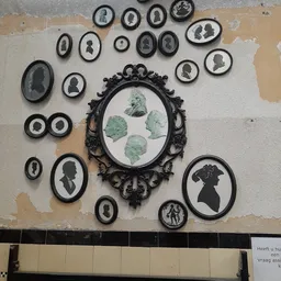 Verzameling zwarte ronde en ovale wanddecoraties met silhouetten en portretjes aan een witte muur