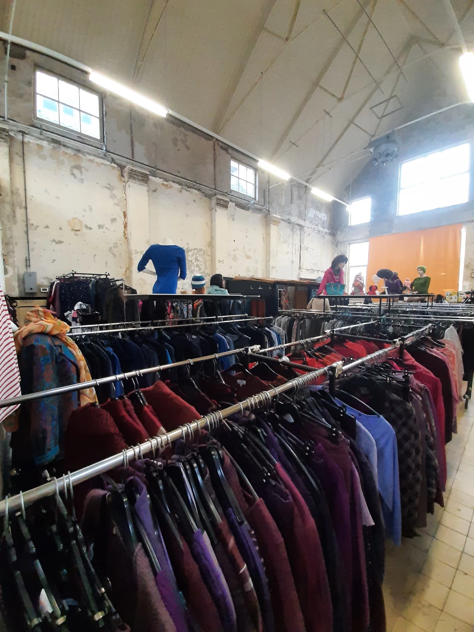 Rekken met tweedehands kleding in diverse kleuren, vooral donkerblauwe en bordeauxrode jassen en jacks