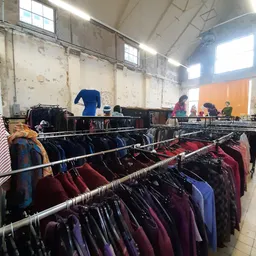 Rekken met tweedehands kleding in diverse kleuren, vooral donkerblauwe en bordeauxrode jassen en jacks