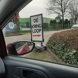 Bord met tekst 'DE KRINGLOOP' en een pijl, gefotografeerd vanuit een auto