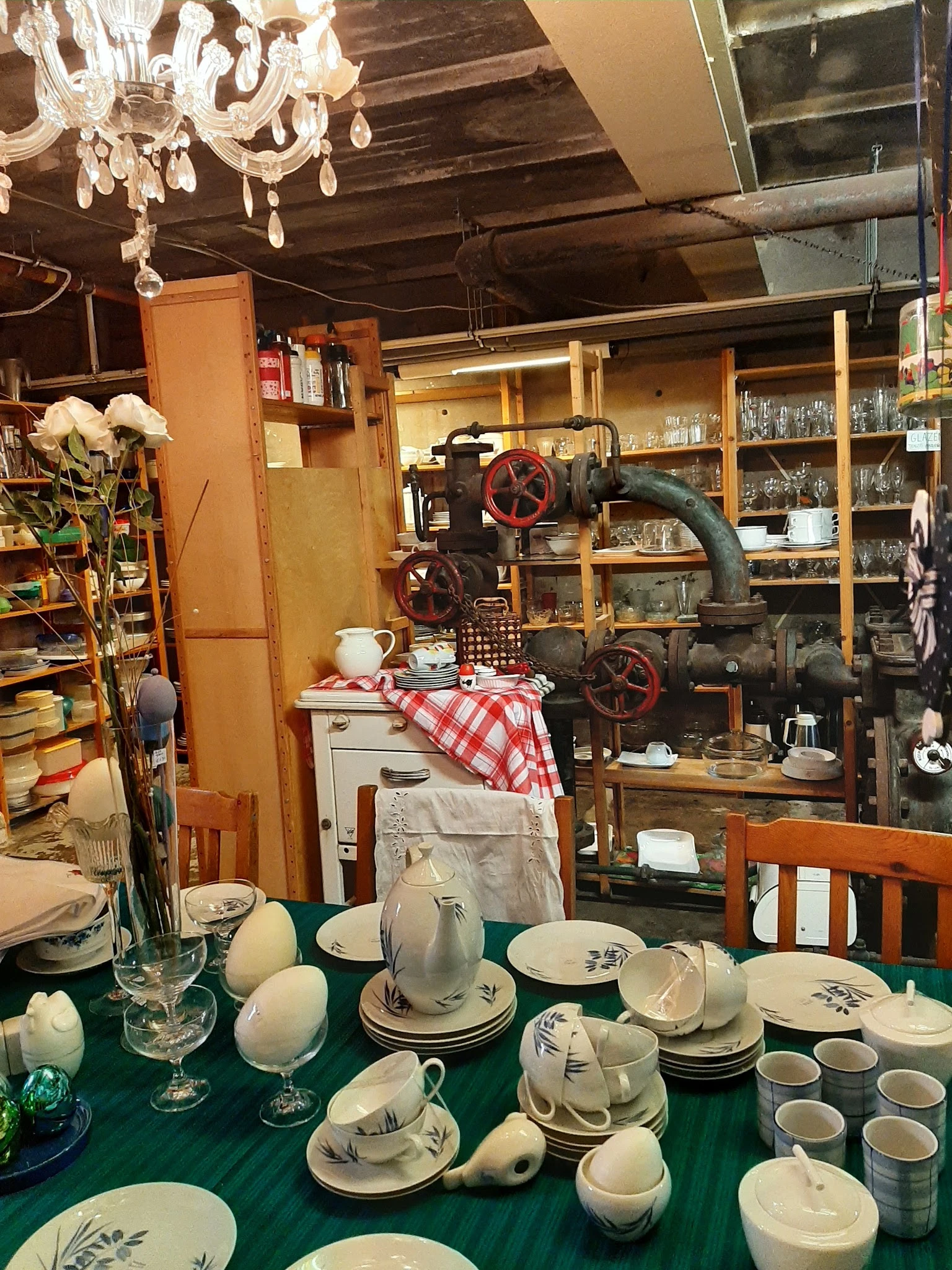 Interieur van kringloopwinkel met vintage servies, industriële machine met wielen en houten stellingen vol spullen