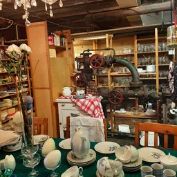 Interieur van kringloopwinkel met vintage servies, industriële machine met wielen en houten stellingen vol spullen