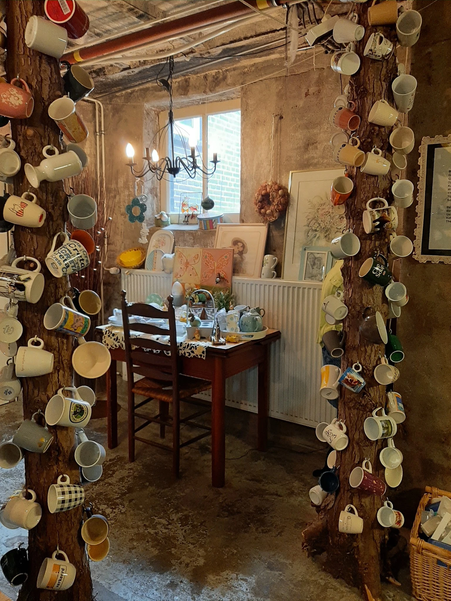 Winkelinterieur met houten wanden behangen met keramische bekers en servies, bureau met inventaris en raam op achtergrond