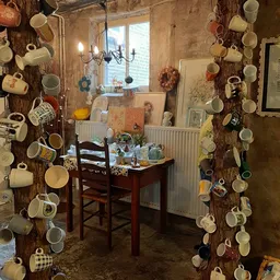 Winkelinterieur met houten wanden behangen met keramische bekers en servies, bureau met inventaris en raam op achtergrond