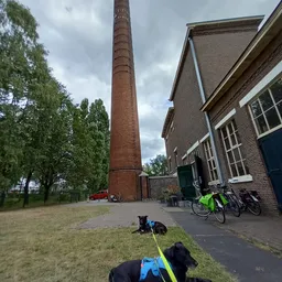 Bakstenen kringloopwinkel met rode schoorsteen, fietsen tegen de gevel en grasveld ervoor