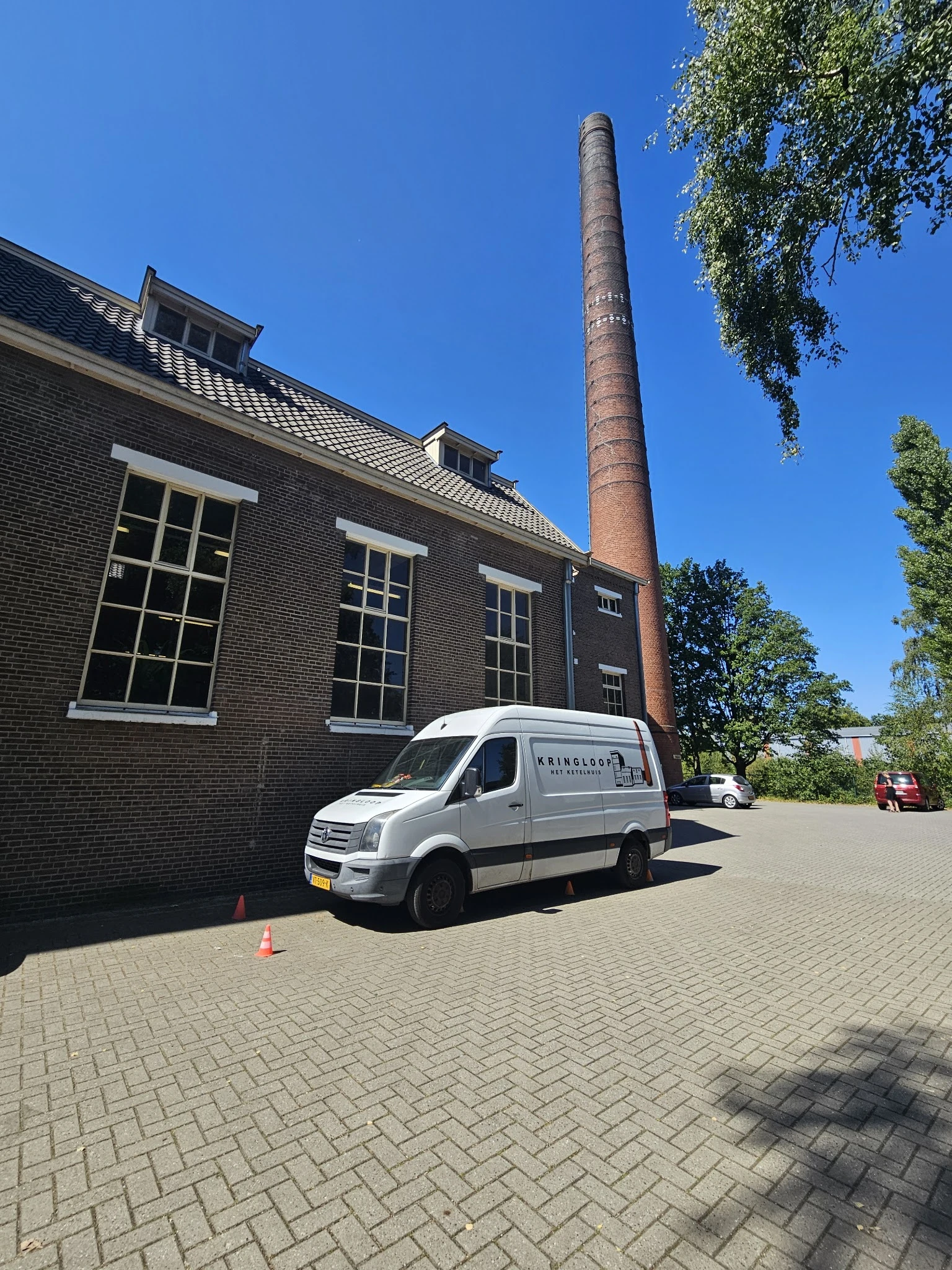 Witte bedrijfsbus met winkelnaam geparkeerd voor bakstenen gebouw met schoorsteen