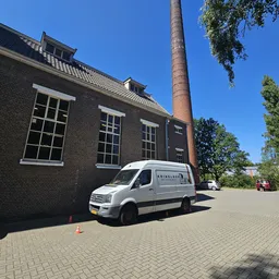 Witte bedrijfsbus met winkelnaam geparkeerd voor bakstenen gebouw met schoorsteen