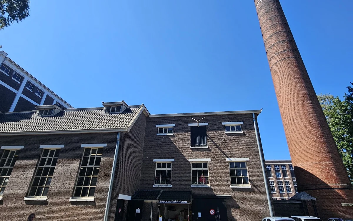 Bakstenen voorgevel van kringloopwinkel Het Ketelhuis met zwarte ingang en ramen, naast hoge rode schoorsteen