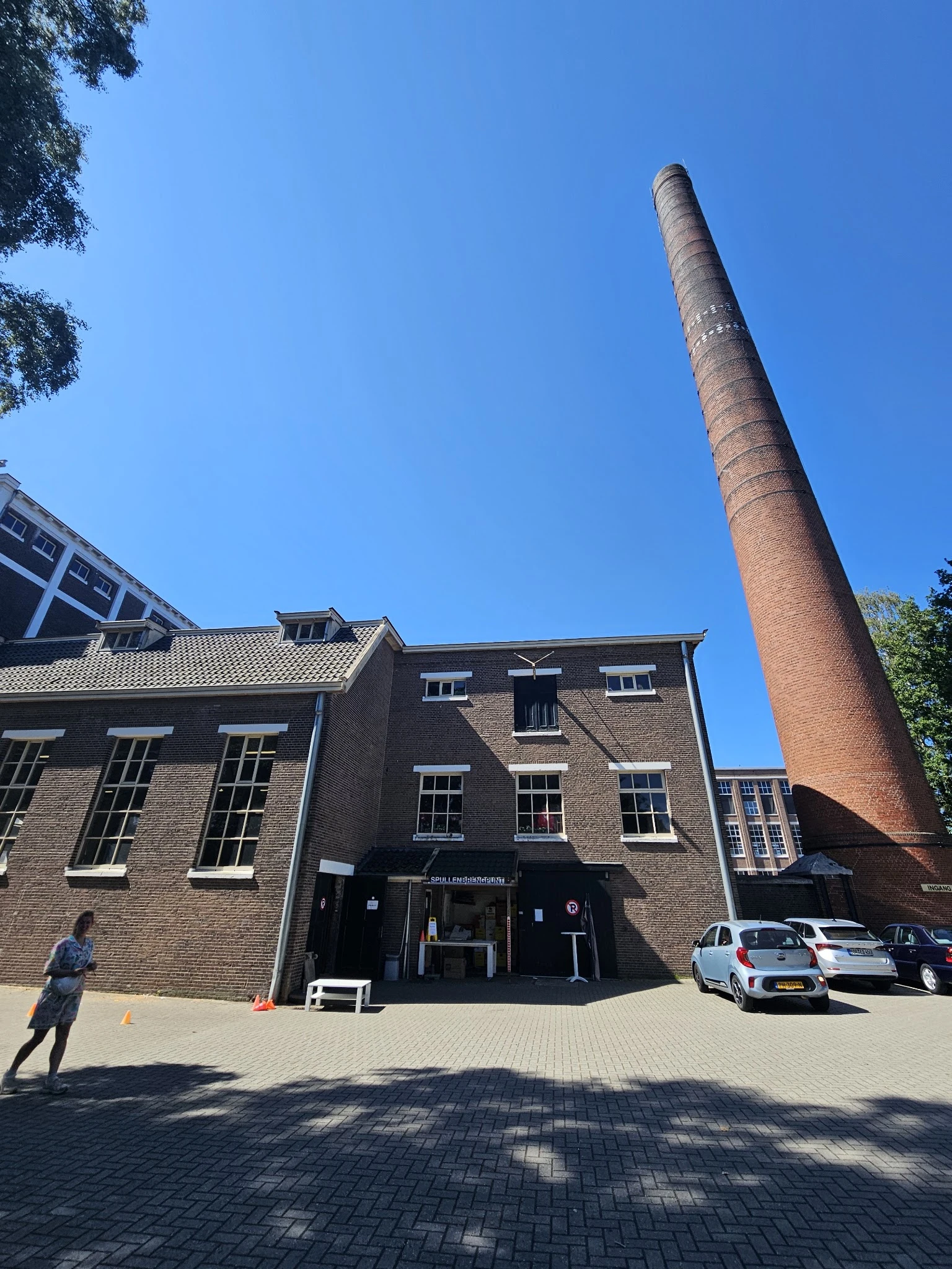 Bakstenen voorgevel van kringloopwinkel Het Ketelhuis met zwarte ingang en ramen, naast hoge rode schoorsteen