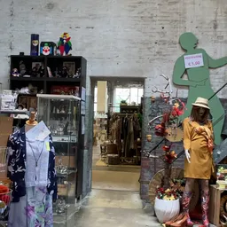 Binnenkant kringloopwinkel met kledinrekken, poppen met kleding, decoratie en displays met spullen