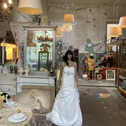 Etalage met bruidsjurk op mannequin, omgeven door decoratiespullen en huishoudartikelen