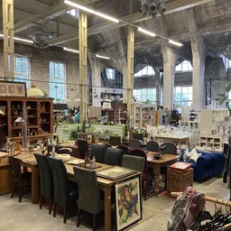 Ruim interieur van kringloopwinkel met houten meubels, tafels, stoelen, kasten en diverse huishoudelijke artikelen tegen grot