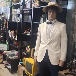 Mannequin gekleed in crèmekleurig colbert met zwarte strik en grijze hoed in een winkel