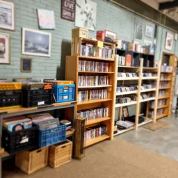 Winkelvloer met houten boekenkast en rekken vol met dvd's en cd's, aan de zijkant enkele dozen en winkelmateriaal