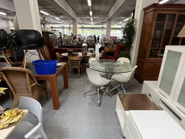 Winkelvloer met diverse meubels: glazen tafel met witte stoelen, houten tafels, stoelen, kasten en andere tweedehands spullen