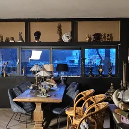 Interieur van kringloopwinkel met eettafel, stoelen, decorstukken en uitzicht op verlichte skyline