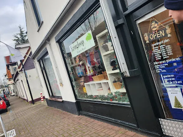 Voorgevel van kringloopwinkel met vitrines, zwarte kozijnen en open bord