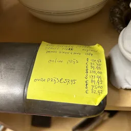 Gele prijssticker op een grijs voorwerp met handgeschreven aantekeningen en prijzen