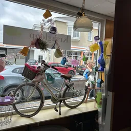 Winkelraam met etalage: fiets, lampen, decoraties en uitzicht op straat met geparkeerde auto's
