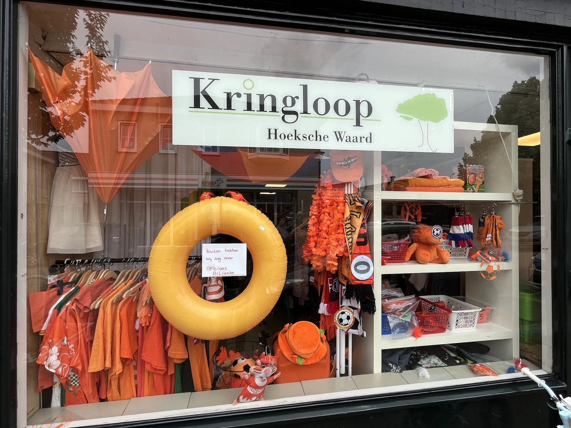 Etalage met oranje en gele kleding, accessoires en decoratieve items uitgestald op planken en aan hangers