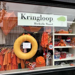 Etalage met oranje en gele kleding, accessoires en decoratieve items uitgestald op planken en aan hangers