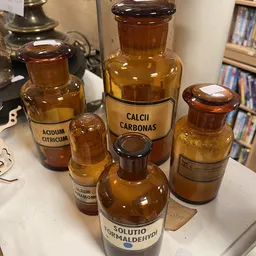 Verzameling antieke apothekersflessen van bruin glas met labels, waaronder Acidum Citricum en Calcii Carbonas