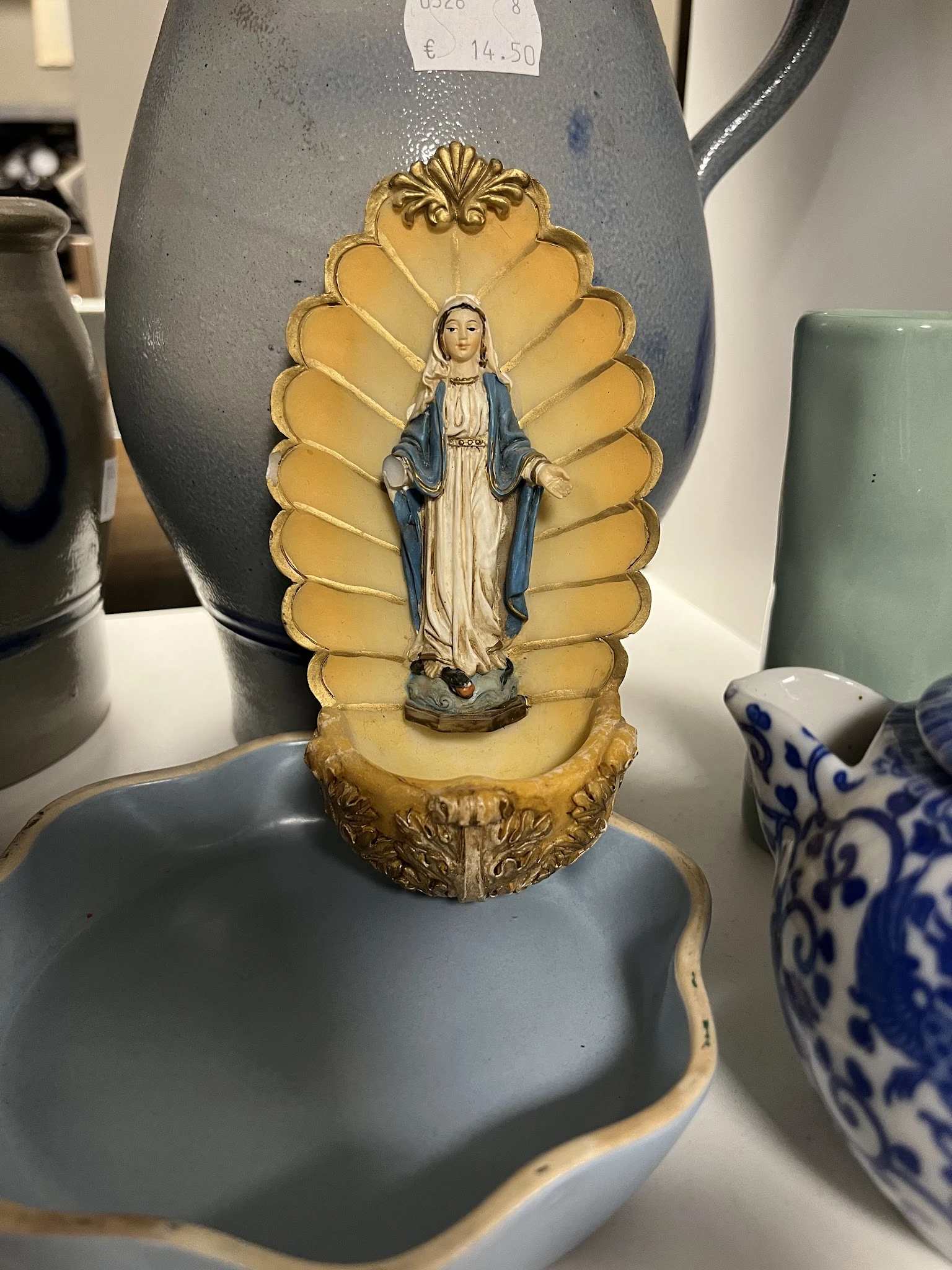 Religieus beeldje van Maria in een gouden aureool, onder glas uitgestald in een kringloopwinkel