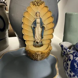 Religieus beeldje van Maria in een gouden aureool, onder glas uitgestald in een kringloopwinkel