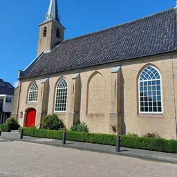 Voorgevel van een bakstenen kerk met rode deur, grote ramen en toren tegen blauwe lucht