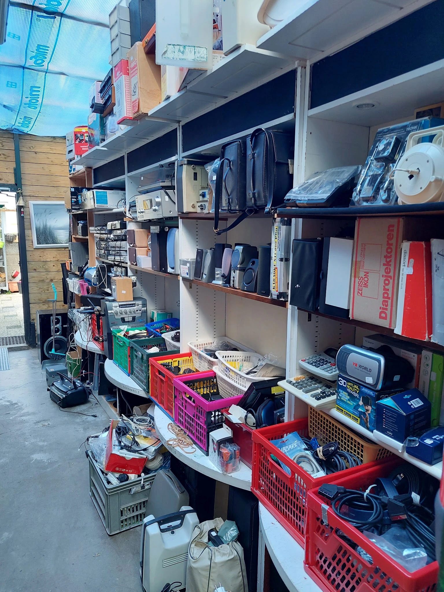 Stellingen met elektronische apparaten, huishoudelijke items en verschillende goederen in een kringloopwinkel